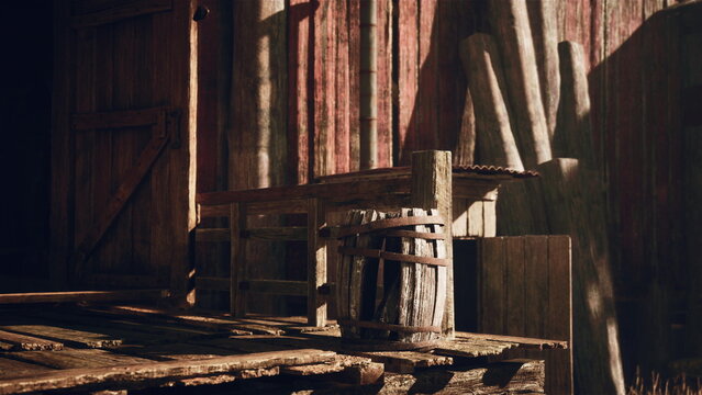 Sunlight filters through the weathered wooden beams, illuminating the aged structures. A barrel sits beside a rustic chair, showcasing the beauty of rural simplicity and history.