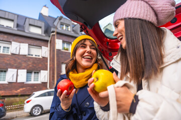 Happy young women sharing apples from car trunk