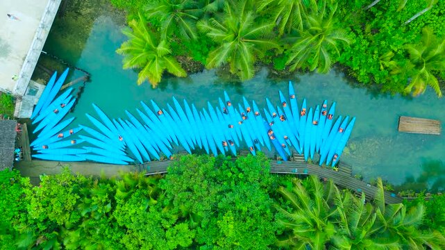 Aerial view of numerous blue kayaks lined up on the Maasin River, surrounded by lush tropical palm trees and green foliage, Siargao, Philippines.
