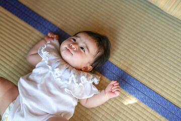 Fototapeta premium A baby is laying on a bed with a blue stripe. The baby is wearing a white dress and has a blue ribbon around its neck