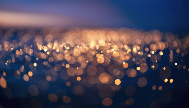 An enchanting abstract background featuring numerous golden bokeh lights softly glowing against a deep blue, dark backdrop. - Powered by Adobe