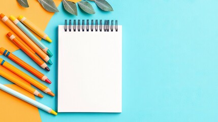 A blank notebook with colorful pencils and leaves arranged on a vibrant orange and blue background, perfect for creative projects and design.