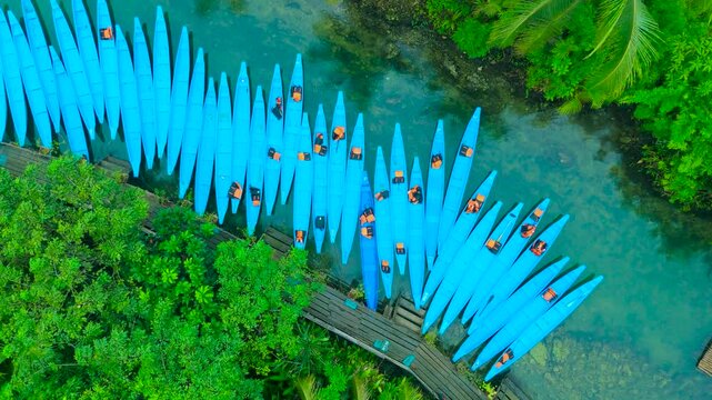 Aerial view of many blue kayaks lined along a wooden dock with people, surrounded by lush palm trees on the Maasin River, Siargao, Philippines.