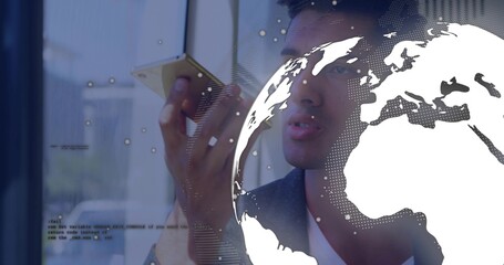Speaking man in dark blazer holding smartphone near mouth at office window, with globe overlay