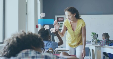 Leaning teacher in yellow blouse white pants high-fiving boy in class right side, desk, copy space