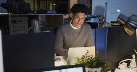 Working office worker in gray sweater white shirt, focusing on laptop in evening with lamp screens