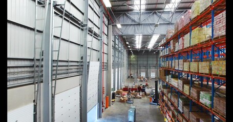 Fototapeta premium Loading staff moving pallets along central aisle in large warehouse, wearing safety vests