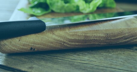 Showing wooden cutting board grain on wooden tabletop, with metal knife black handle and greens © vectorfusionart