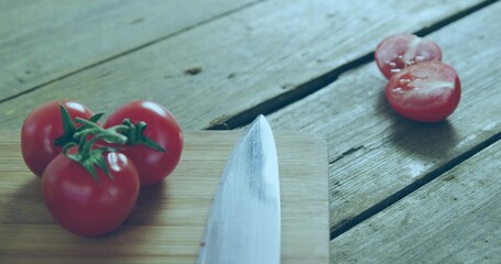 Showing three vine tomatoes on cutting board at kitchen table with knife, halved tomato, copy space