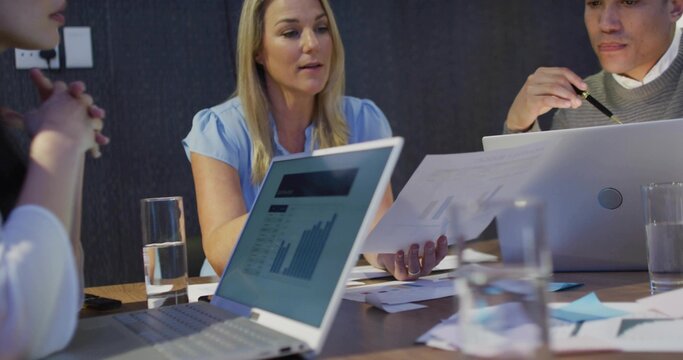 Reviewing charts, blonde woman in blue blouse and gray-sweater man using laptops at meeting table