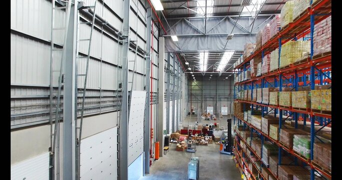 Loading staff moving pallets along central aisle in large warehouse, wearing safety vests