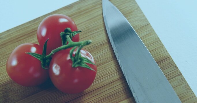 Shining 3 cherry tomatoes with green stems sitting on board in kitchen, serrated knife, copy space