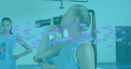 Drinking blonde athlete lifting black sports bottle on gym court, with blue jerseys, hoop, overlays