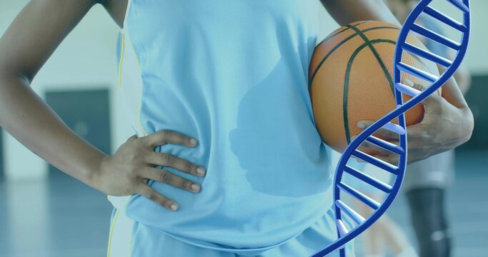 Holding orange basketball, player in light blue jersey, shorts posing at gym with blue DNA overlay - Powered by Adobe