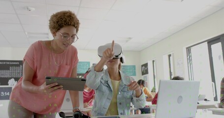 Pointing student wearing denim jacket and yellow top engaging in class with VR headset and tablet
