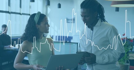 Discussing colleagues holding laptop and tablet in open office, displaying line-graph overlay