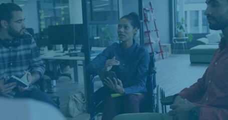 Speaking woman holding tablet and stylus in wheelchair at open-plan office, wearing blue shirt © vectorfusionart