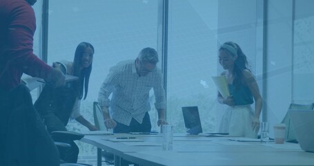 Reviewing papers, four colleagues leaning over table in meeting room with laptop and checked shirt