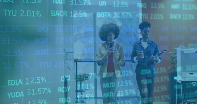 Walking two business-casual women viewing financial overlay in hall, holding phone, tablet, coffee