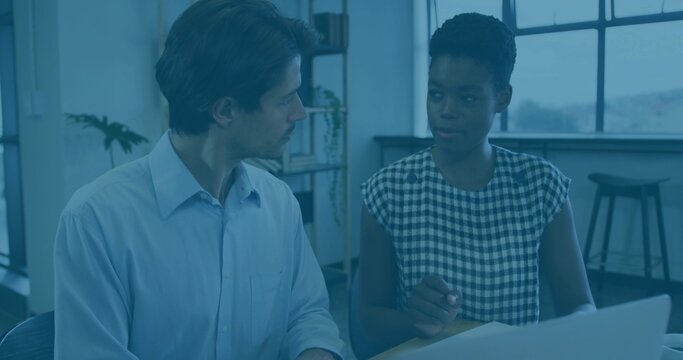 Reviewing documents, woman in gingham dress and man in button-down talking at office with laptop