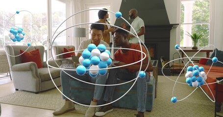 Naklejka premium Studying two men sitting on sofa using tablet in living room with floating molecular models