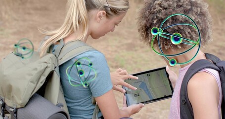 Pointing, two women checking tablet map on dirt trail, wearing blue pink tops, packs, neon overlays