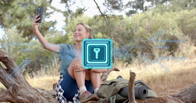 Sitting woman holding phone for selfie on fallen log in woodland, digital key icon, checked shirt