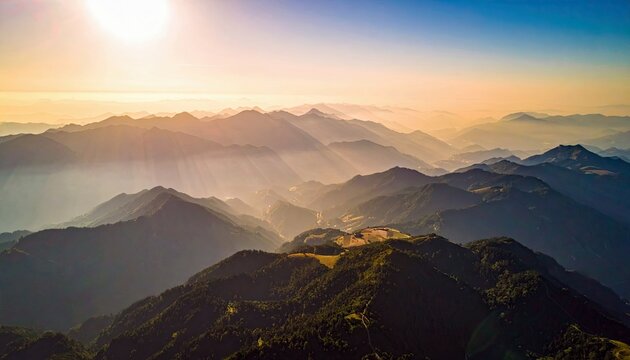 Aerial view of a mountain range at sunrise. The sun casts a golden glow over the peaks and valleys, creating a serene and majestic landscape.