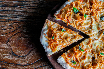 Top-down view of spaghetti pizza slices with melted cheese and basil on a rustic wooden table. Appetizing fusion food background with copy space, perfect for menus, restaurants, and food marketing.