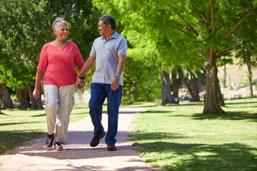 Senior, happy couple and holding hands with walk in park for bonding, fresh air or outdoor together. Elderly, man or woman with smile on path or trail for holiday, weekend or retirement in nature