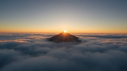 Mountain peak rising above the clouds at sunrise with sun rays