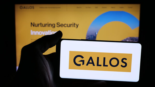 Stuttgart, Germany - 11-24-2025: Person holding mobile phone with logo of British company Gallos Technologies Ltd. on screen in front of web page. Focus on phone display.