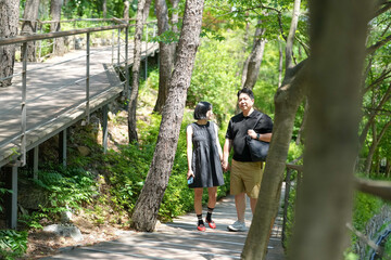 Fototapeta premium A man and woman are walking on a path in a forest. The man is carrying a backpack and the woman is holding his hand. Scene is peaceful and romantic, as the couple enjoys their time together in nature