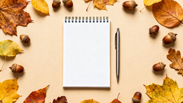 Blank notepad with pen on beige background surrounded by autumn leaves and acorns, seasonal workspace and writing concept  