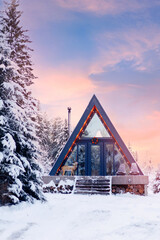 Glamping aframe cabin in snowy forest at sunset with christmas lights and reindeer decor