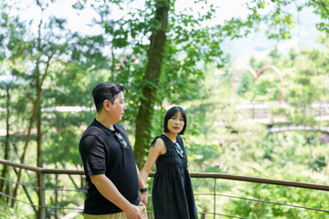 Fototapeta premium A man and a woman are standing on a bridge in a forest. The man is holding the woman's hand