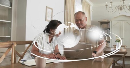 Mature man placing laptop and senior woman marking papers in dining, globe orbiting finance data - Powered by Adobe