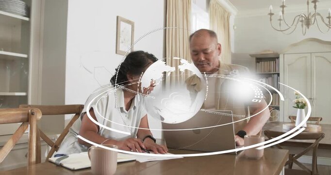 Mature man placing laptop and senior woman marking papers in dining, globe orbiting finance data - Powered by Adobe