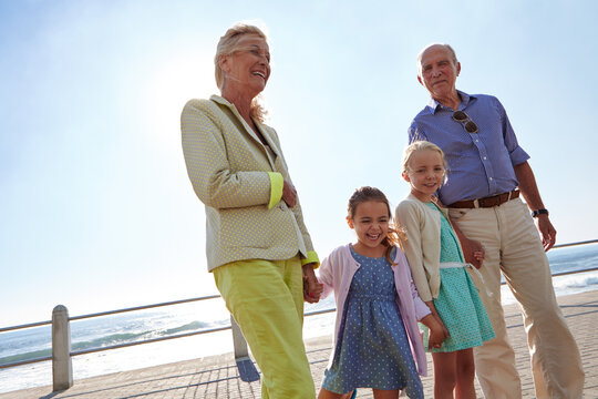 Grandparents, grandchildren and holding hands on beach promenade for walk, happiness or bonding together. Grandma, grandpa and grandkids outdoor by ocean with stroll for portrait, space or low angle.