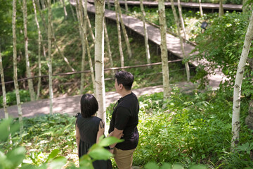 A couple is walking through a forest, holding hands and looking at the trees. Scene is peaceful and romantic