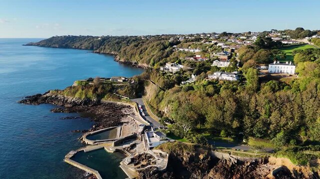 High distant drone footage along coastline of Havelet Bay Guernsey seawater bathing pools,Fort George Clarence Battery views along coast and across the Island on calm day in late afternoon sunshine