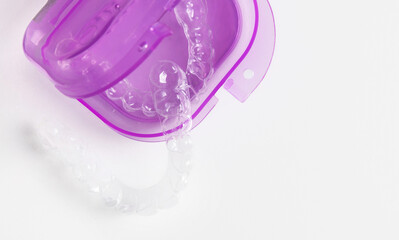 Woman holds whitening trays and solution on a minimal backdrop. Clear trays, dental model, case and syringes placed on the table. The woman applies gel into the trays for tooth care and bright smile.