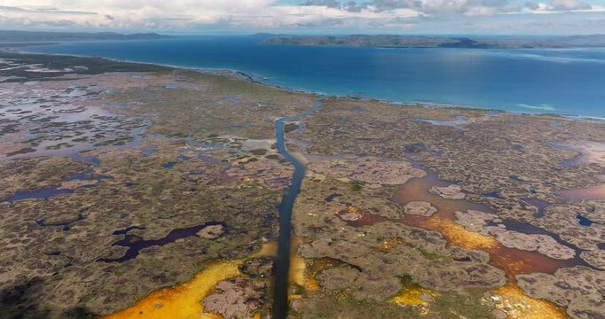 Aerial drone view of a waterway channel cutting through the totora reeds of the Uros floating islands on Lake Titicaca near Puno, Peru. The vast lake and Andes mountains stretch into the distance