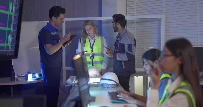 Engineers in high visibility vests collaborate in control room, reviewing digital site plans and dashboards during an operations and safety discussion. Coordination, monitoring, and incident readiness