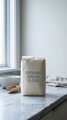 Brown paper bag labeled organic bread flour sits on a marble countertop beside a wooden spoon and a ceramic bowl, creating a cozy kitchen atmosphere for baking enthusiasts