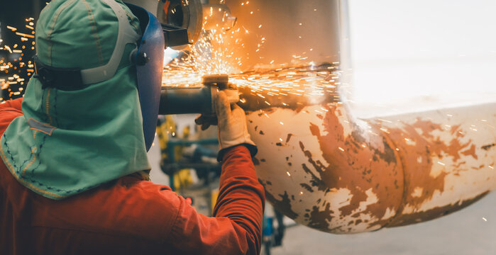 A welder is focused on cutting and shaping a metal pipe in an industrial workshop. Bright sparks fly as the equipment is used, showcasing the intensity and skill of the task