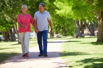 Senior, happy couple and holding hands in park for bonding, fresh air or outdoor walk together. Elderly, man or woman with smile on path or trail for holiday, weekend or retirement in nature or woods