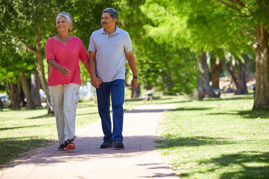 Senior, happy couple and holding hands in park for bonding, fresh air or outdoor walk together. Elderly, man or woman with smile on path or trail for holiday, weekend or retirement in nature or woods - Powered by Adobe