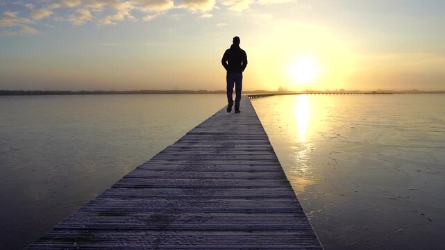 A man walking on a jetty (Knuppelpad) in nature reserve Roegwold during a cold, autumn sunrise.