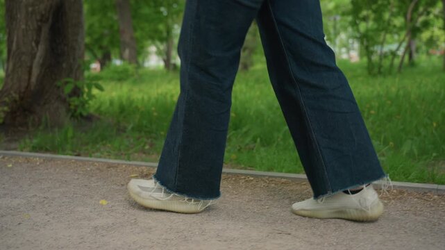 she walks relaxedly through greenery, casual woman in denim traverses park path surrounded by greenery, an individual in casual attire walks steadily along treelined park trail during summer